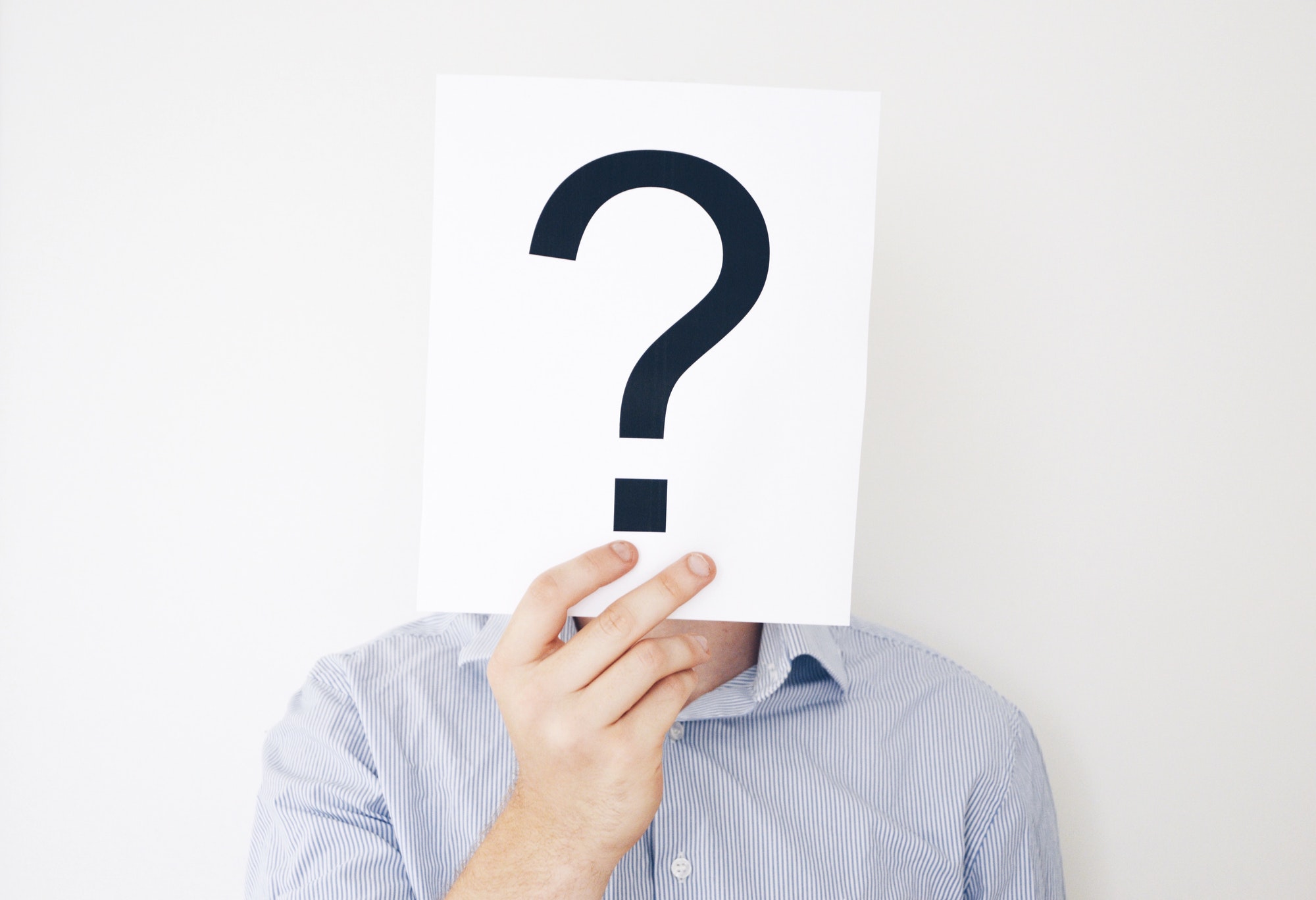 A man wearing a light blue shirt holding a question mark in front of his head